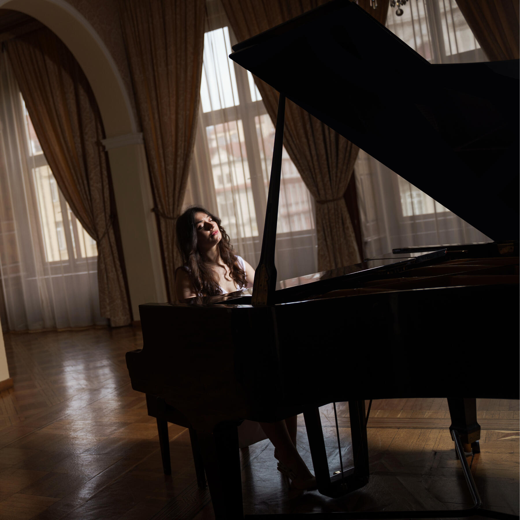 Choirmaster Jennifer Evans at the piano A dark-haired woman sits with closed eyes in front of a grand piano, enthralled with the music.